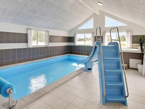 An indoor swimming pool with two slides, a ladder, and a view of the outdoors through large windows. - 5 Star Holiday Home in Vejby (Vejby)
