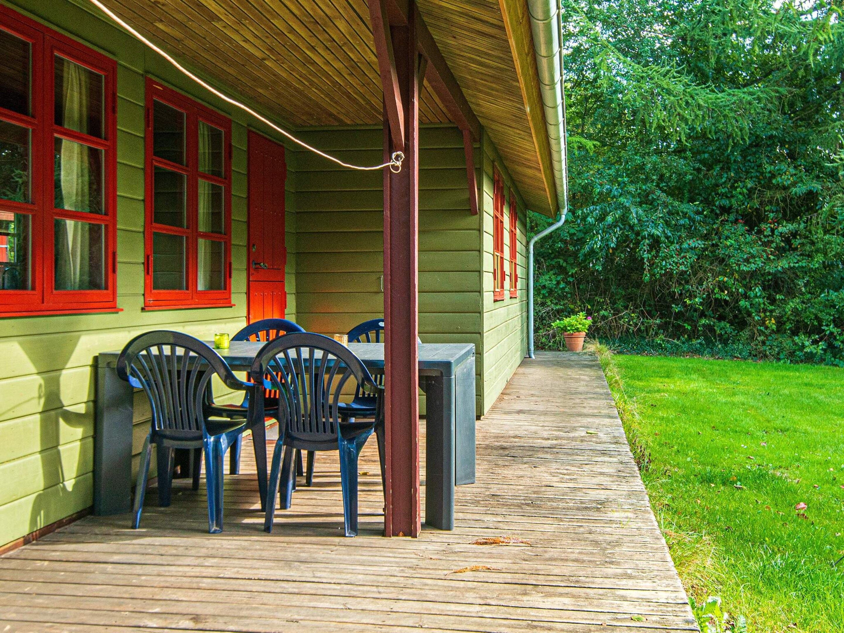 A wooden deck with a table and chairs, a covered area with a roof, and a green lawn.