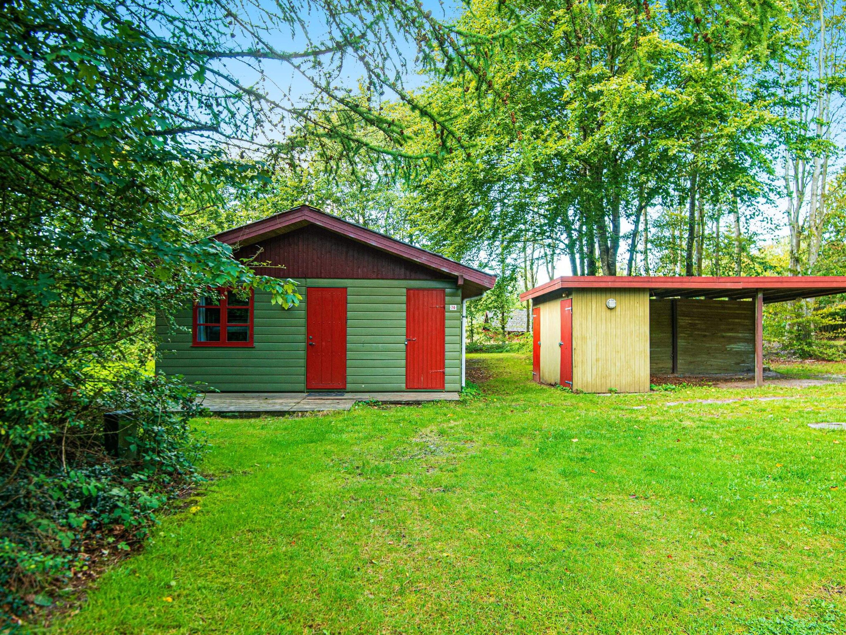A small, single-story building with a red door and a green exterior, surrounded by lush greenery and trees.