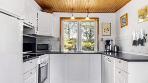 A kitchen with white cabinets, a microwave, an oven, a coffee maker, and a window with a view of trees. - 4 Star Holiday Home in Jerup (Jerup)