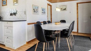 A modern kitchen with white cabinets, a dining area with a round table and black chairs, and wooden ceiling beams. - 4 Star Holiday Home in Jerup (Jerup)
