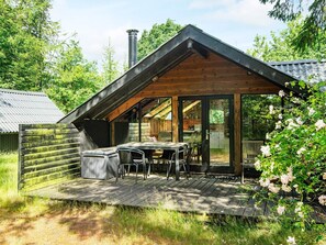 Eine Holzhütte mit geneigtem Dach, einer Terrasse mit Gartenmöbeln und einem Schornstein.