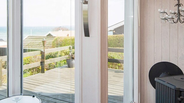 Una stanza con un'ampia porta in vetro che si apre su un terrazza in legno con vista sul mare.