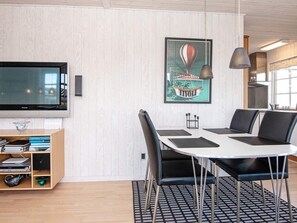 A modern living room with a flat-screen TV, a wooden entertainment unit, a dining table with chairs, and a framed artwork on the wall. - Seaside Escape With Views - By Traum Ferienwohnungen (Hejls)