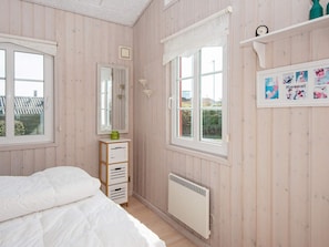 A bedroom with wooden walls, a bed, a dresser, a radiator, and a window with a view of the outside. - Seaside Escape With Views - By Traum Ferienwohnungen (Hejls)