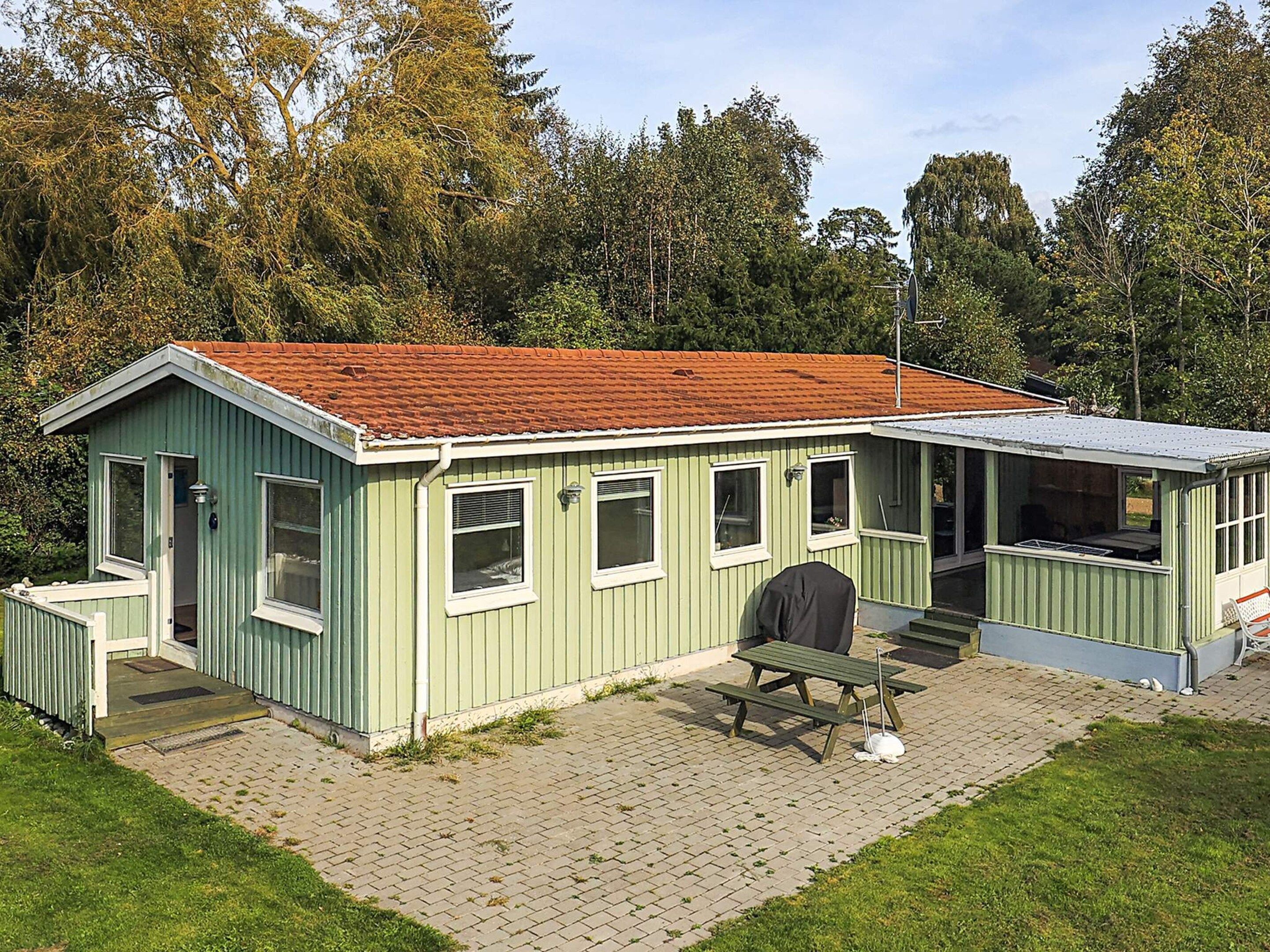 A small, single-story building with a red-tiled roof, a covered porch, and a picnic table.