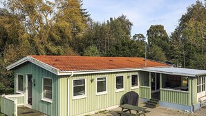 A small, single-story building with a red-tiled roof, a covered porch, and a picnic table. - 8 Person Holiday Home in Stege (Stege)