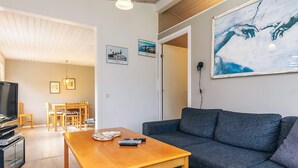 A modern living room with a wooden coffee table, grey sofa, and a television. There are framed pictures on the wall and a painting above the sofa. - 8 Person Holiday Home in Stege (Stege)