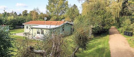 Une maison de plain-pied avec un toit recouvert de tuiles rouges, entourée d’une pelouse bien entretenue et d’arbres.
