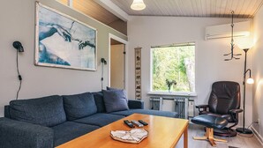 A modern living room with a grey sofa, a wooden coffee table, a black leather chair, and a large window with a view of greenery. - 8 Person Holiday Home in Stege (Stege)