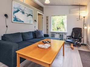 Un salon moderne avec un canapé gris, une table basse en bois, un fauteuil en cuir noir et une grande fenêtre donnant sur un paysage verdoyant.