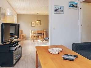 A living room with a TV, wooden furniture, and a table with remote controls.