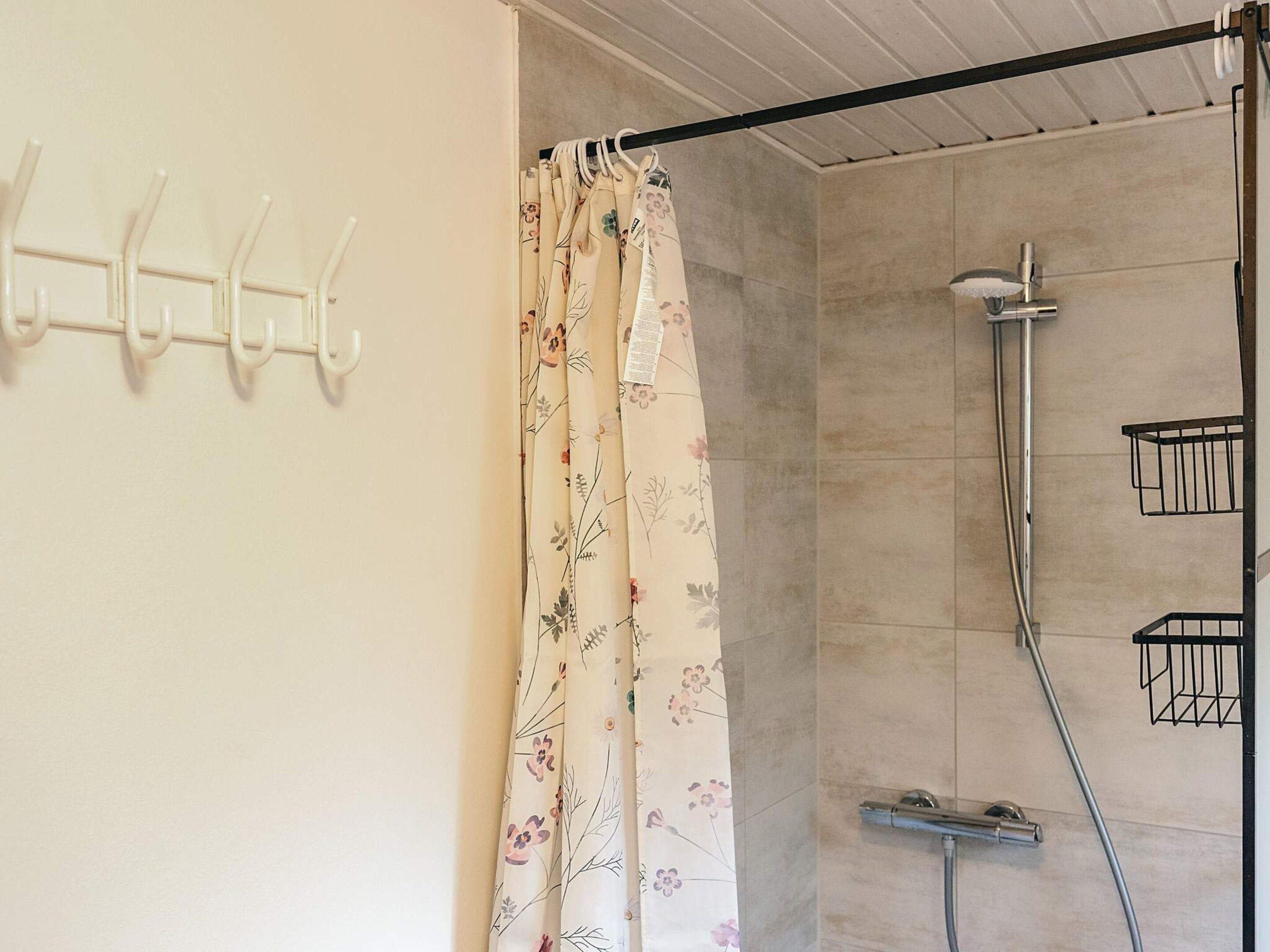 Une salle de bain avec une douche, un rideau à motifs floraux et un porte-serviettes avec des crochets.
