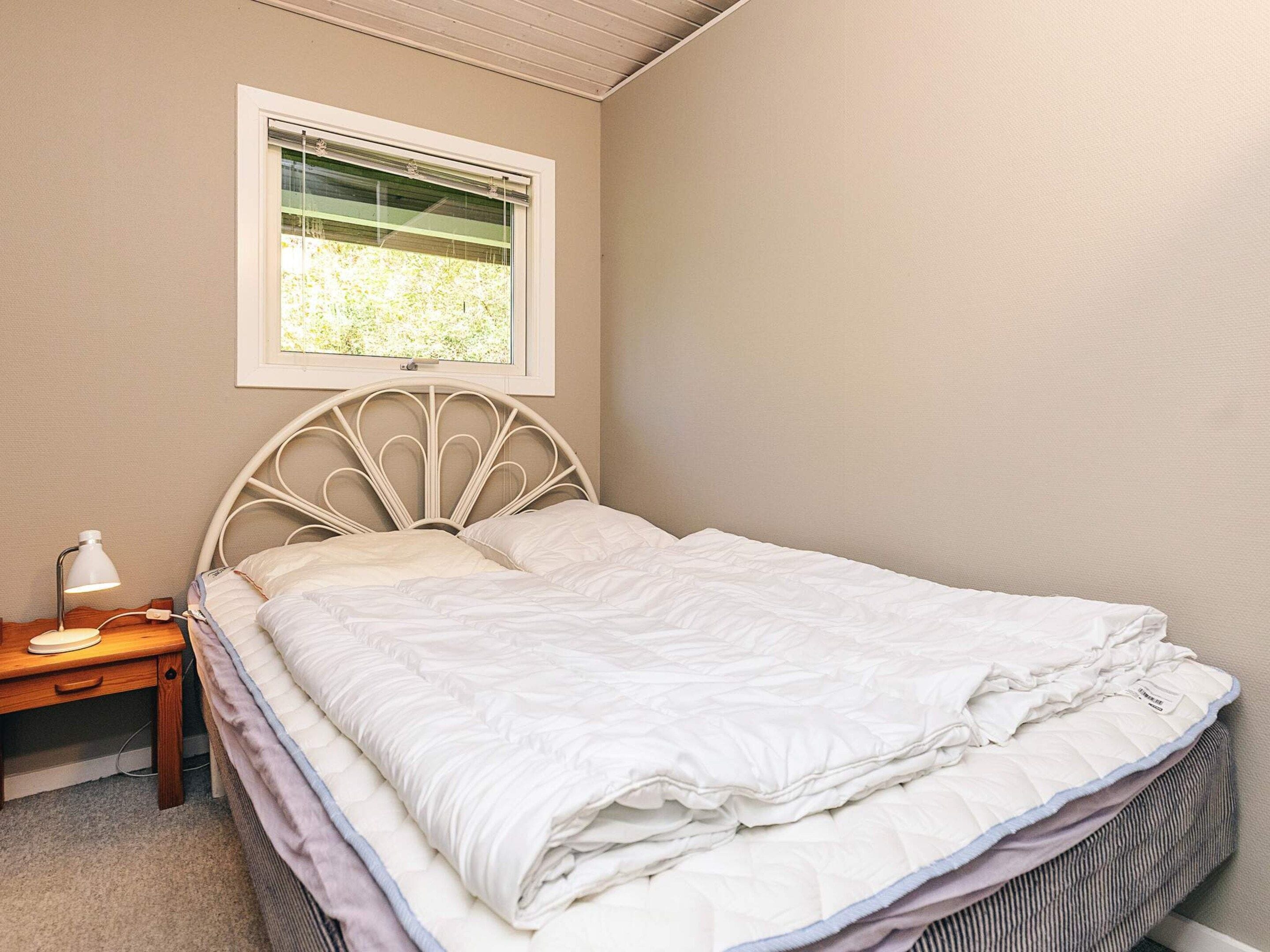 A neatly made bed with a headboard, a bedside table with a lamp, and a window above the bed.