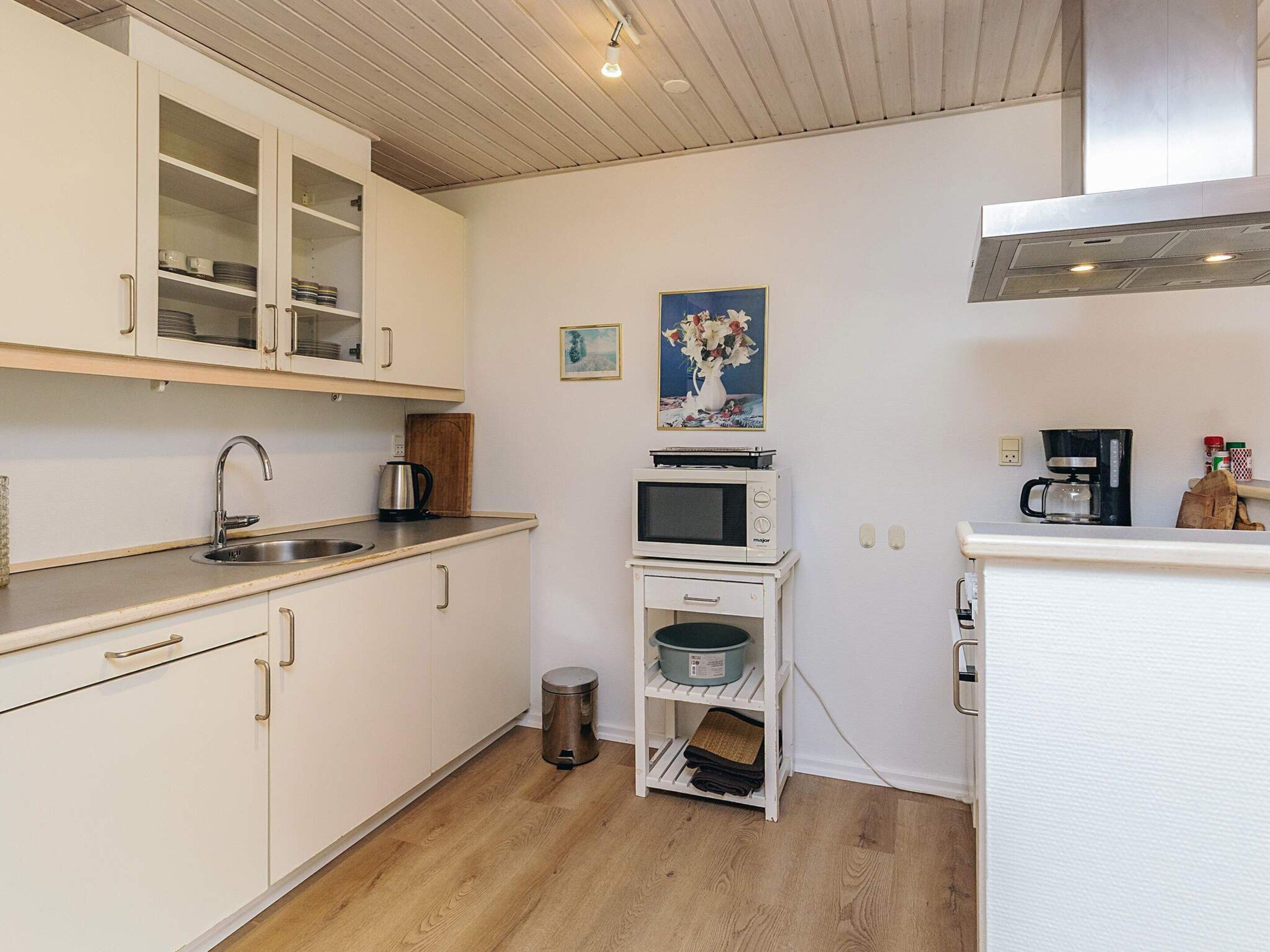 A compact kitchen with white cabinets, a stainless steel sink, a microwave, a coffee maker, and a trash bin.