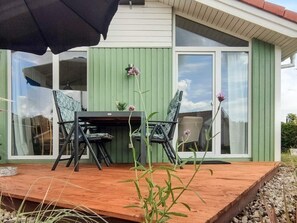 An outdoor patio with a table and chairs, a green wall, and a window.