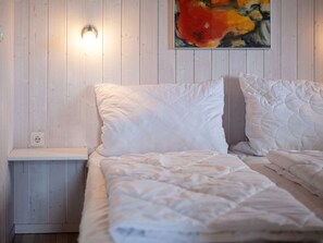 A bedroom with a bed, a nightstand, a wall socket, and a painting. - Holiday Home in GrÃ¶mmitz (Groemitz)