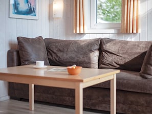 A modern living room with a brown leather sofa, a wooden coffee table, and a window with curtains. - Holiday Home in GrÃ¶mmitz (Groemitz)