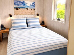 A bed with striped bedding, a painting of a beach scene, and a window with a view of greenery.