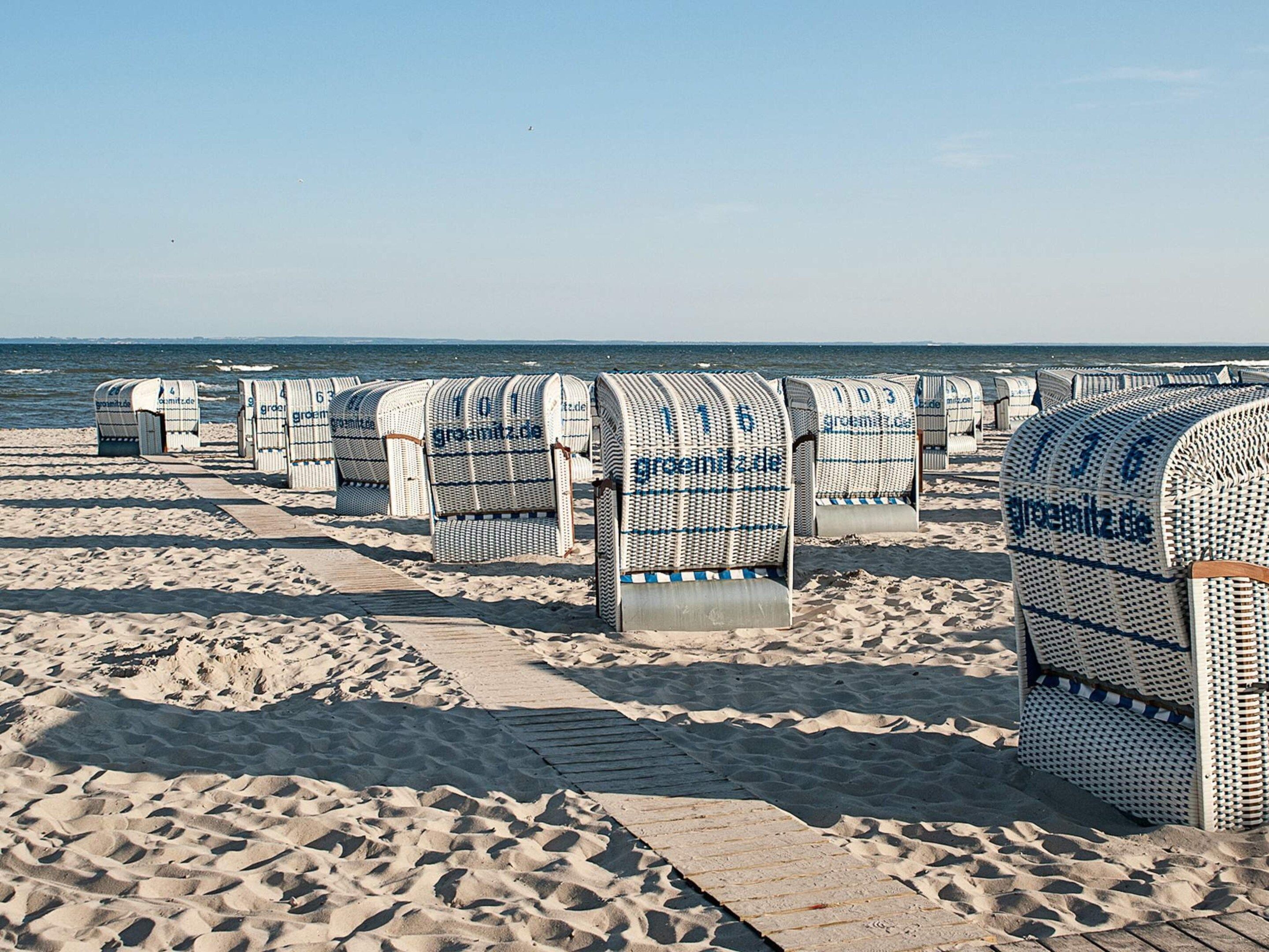 Beach huts with numbers on them, arranged in rows on a sandy beach with the sea in the background.