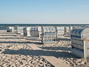 Beach huts with numbers on them, arranged in rows on a sandy beach with the sea in the background. - Holiday Home in GrÃ¶mmitz (Groemitz)