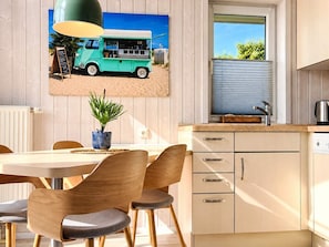 A dining area with a table, chairs, a potted plant, and a kitchen with cabinets and a window.