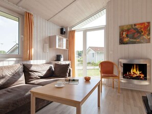 A cozy living room with a sofa, a table, a fireplace, and a painting on the wall. - Holiday Home in GrÃ¶mmitz (Groemitz)