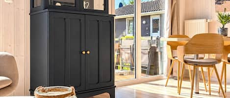 Een modern interieur met een zwarte kast, een eethoek met houten stoelen en een glazen pot met schelpen op een tafel.