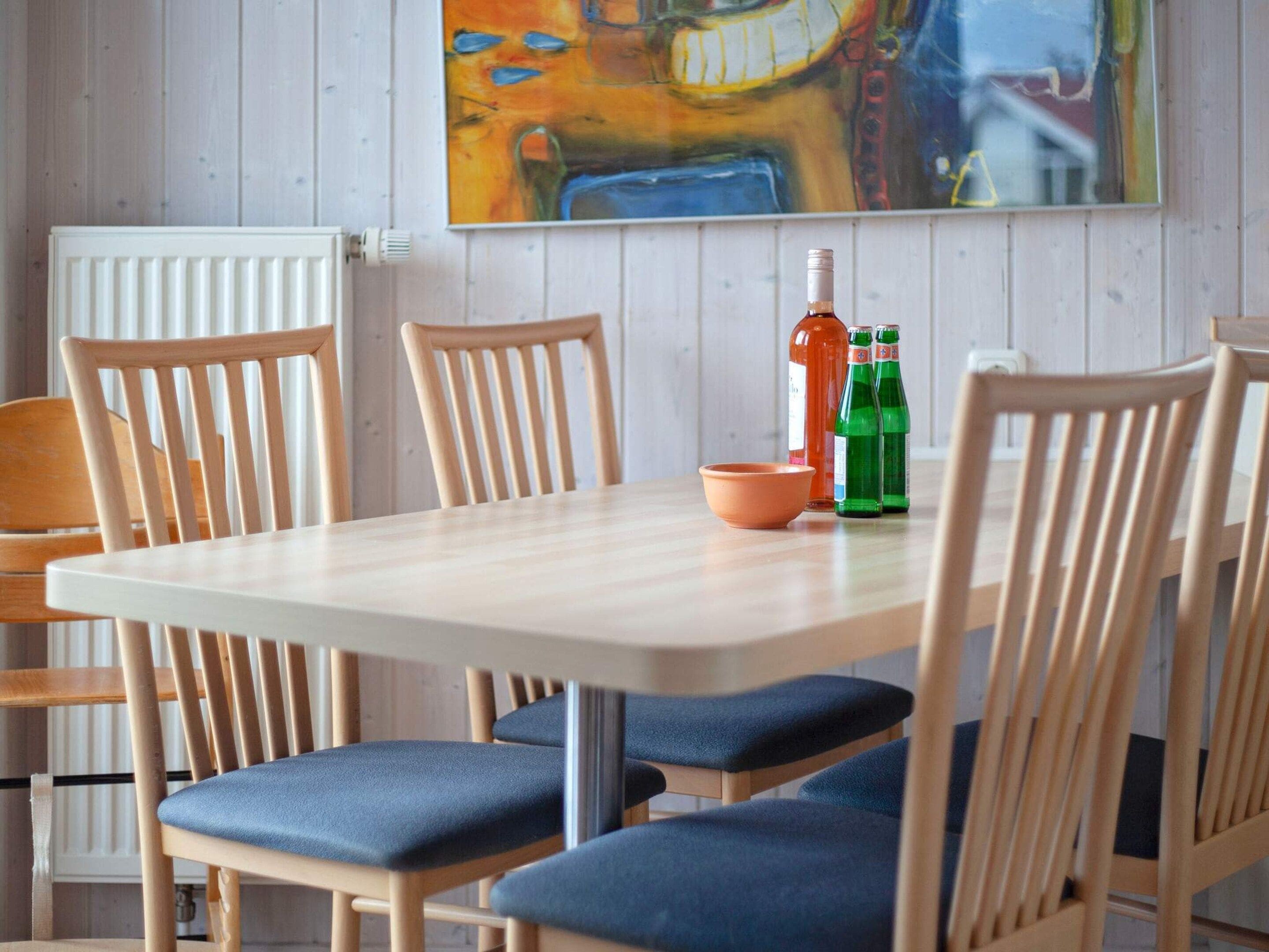 A dining area with a white table, wooden chairs with blue cushions, and a painting on the wall.