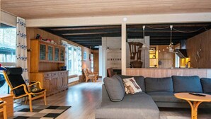 A spacious living area with a grey sectional sofa, wooden flooring, and a kitchen area with wooden cabinets and a dining table. - Tranquil Holiday Home in Glesborg with Hot Tub & Sauna (Glesborg)