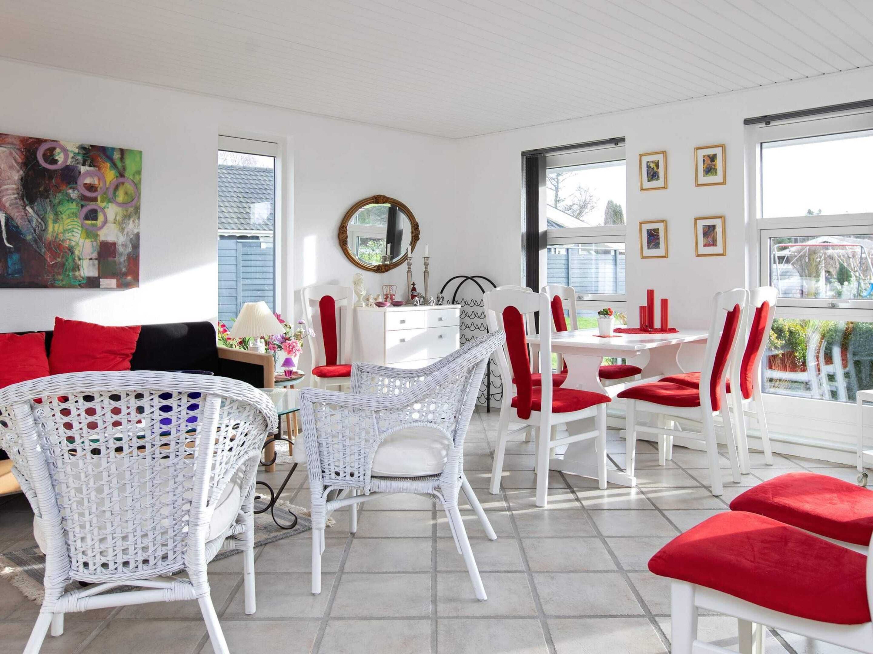 A bright, well-lit room with white wicker furniture, red cushions, and a dining area with white chairs and a table.