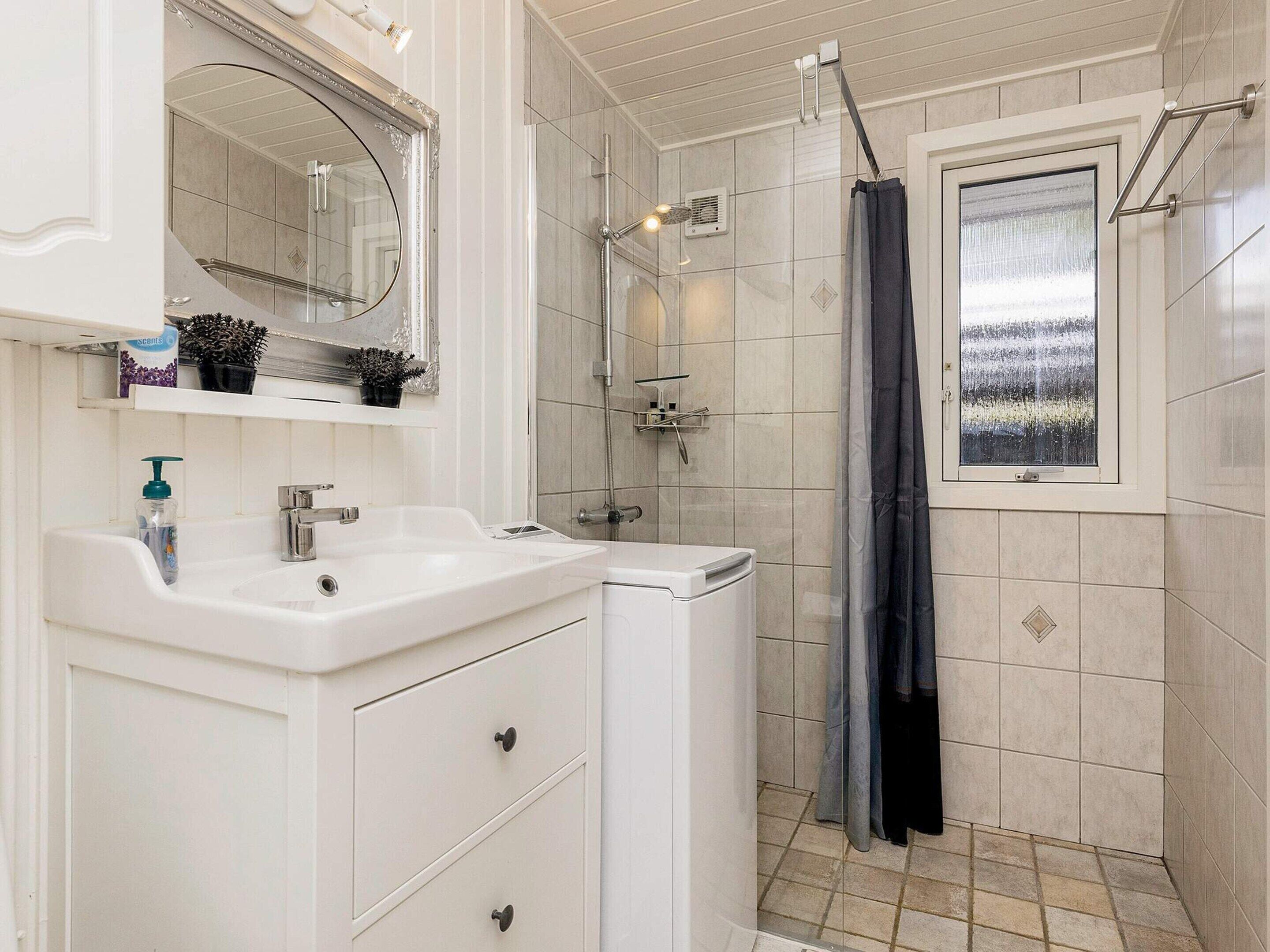 Une salle de bain avec un meuble-lavabo blanc, un miroir, un espace douche et une fenêtre donnant sur un beau paysage.