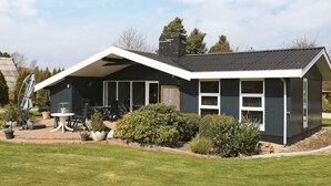 Ein modernes Haus mit Satteldach, großen Fenstern und einer Terrasse mit Gartenmöbeln.