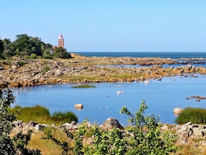A coastal landscape with a rocky shoreline, a body of water, and a lighthouse in the distance.
