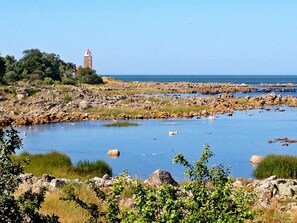 Eine Küstenlandschaft mit felsigem Ufer, einem Gewässer und einem Leuchtturm in der Ferne.