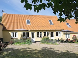 A two-story building with a tiled roof, a picket fence, and a garden area with a table and chairs. - 4 Person Holiday Home in Svaneke (Svaneke)