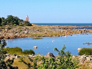 A coastal landscape with a rocky shoreline, a body of water, and a lighthouse in the distance. - 4 Person Holiday Home in Svaneke (Svaneke)