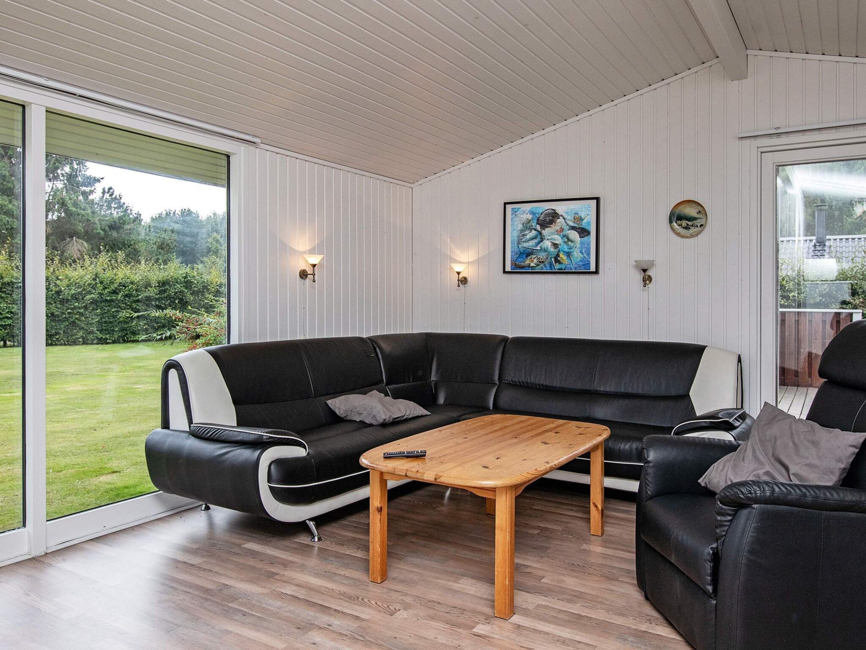 A modern living room with a black leather sectional sofa, a wooden coffee table, and a large sliding glass door leading to a garden.