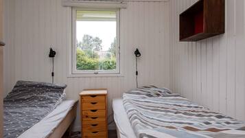 A bedroom with two single beds, a wooden dresser, and a window with a view of greenery.