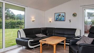 A modern living room with a black leather sectional sofa, a wooden coffee table, and a painting on the wall.