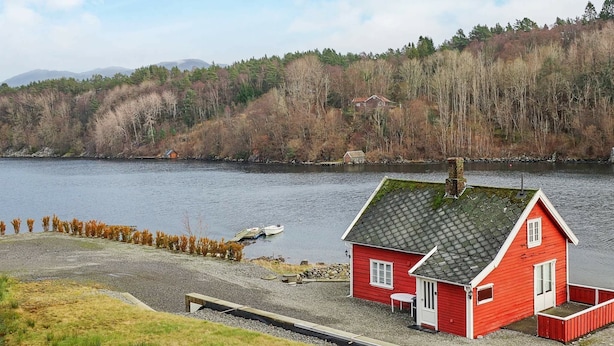 Une maison rouge avec un quai au bord d’un lac, entourée d’arbres et de collines.