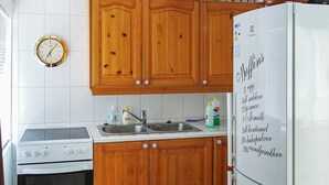 Une cuisine avec des meubles en bois, un fourneau blanc, un évier et un réfrigérateur sur lequel est affichée une liste de courses.
