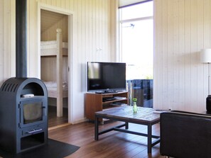 A room with a wood-burning stove, a television on a wooden stand, a table with a vase, and a bunk bed in the background. - 6 Person Holiday Home in Lemvig (Lemvig)