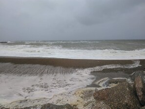A beach with waves crashing onto the shore and a cloudy sky.