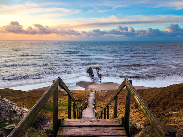 A wooden staircase leading to a beach with a view of the ocean and a cloudy sky.