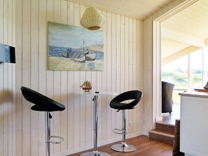 A room with a painting of a sailing scene, two bar stools, a small table, and a wicker lamp.