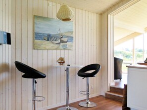 A room with a painting of a sailing scene, two bar stools, a small table, and a wicker lamp. - 6 Person Holiday Home in Lemvig (Lemvig)