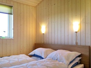 Habitació amb parets de fusta, un llit amb roba de llit blanca i dues làmpades fixes a la paret.
