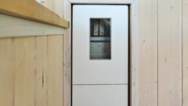 Una porta blanca amb un petit finestre, revestiment de fusta a les parets i un nínxol de fusta sobre la porta.