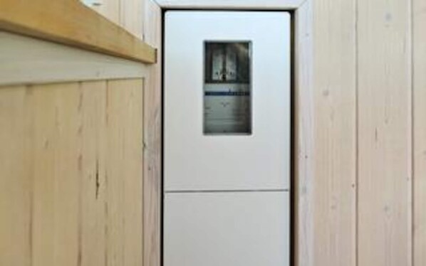 Une porte blanche avec une petite fenêtre, des lambris en bois sur les murs et une étagère en bois au-dessus de la porte.